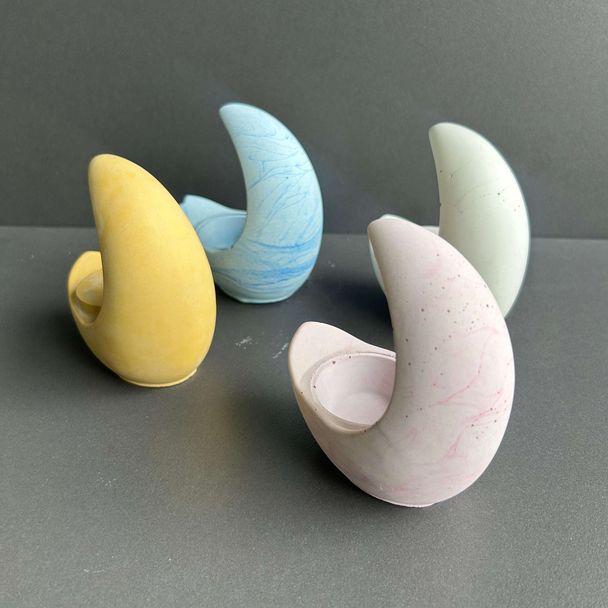 Set of colorful concrete moon-shaped candle holder on a gray surface